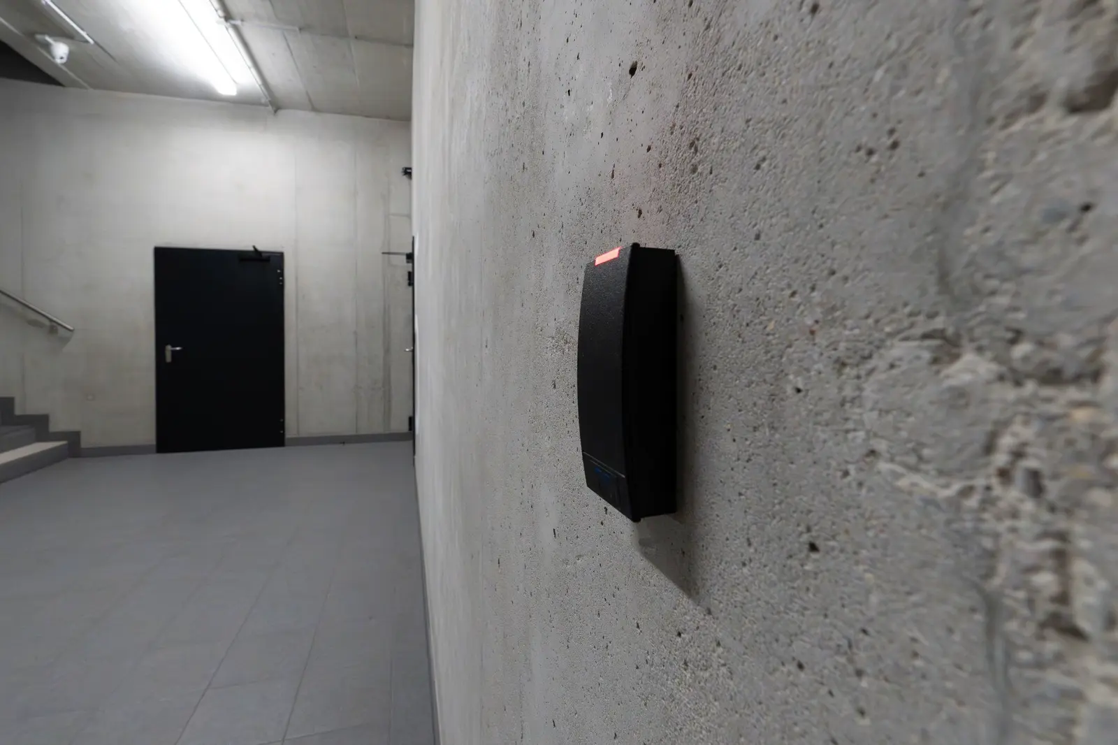 An unbranded badge reader on a concrete wall in a secured corridor.