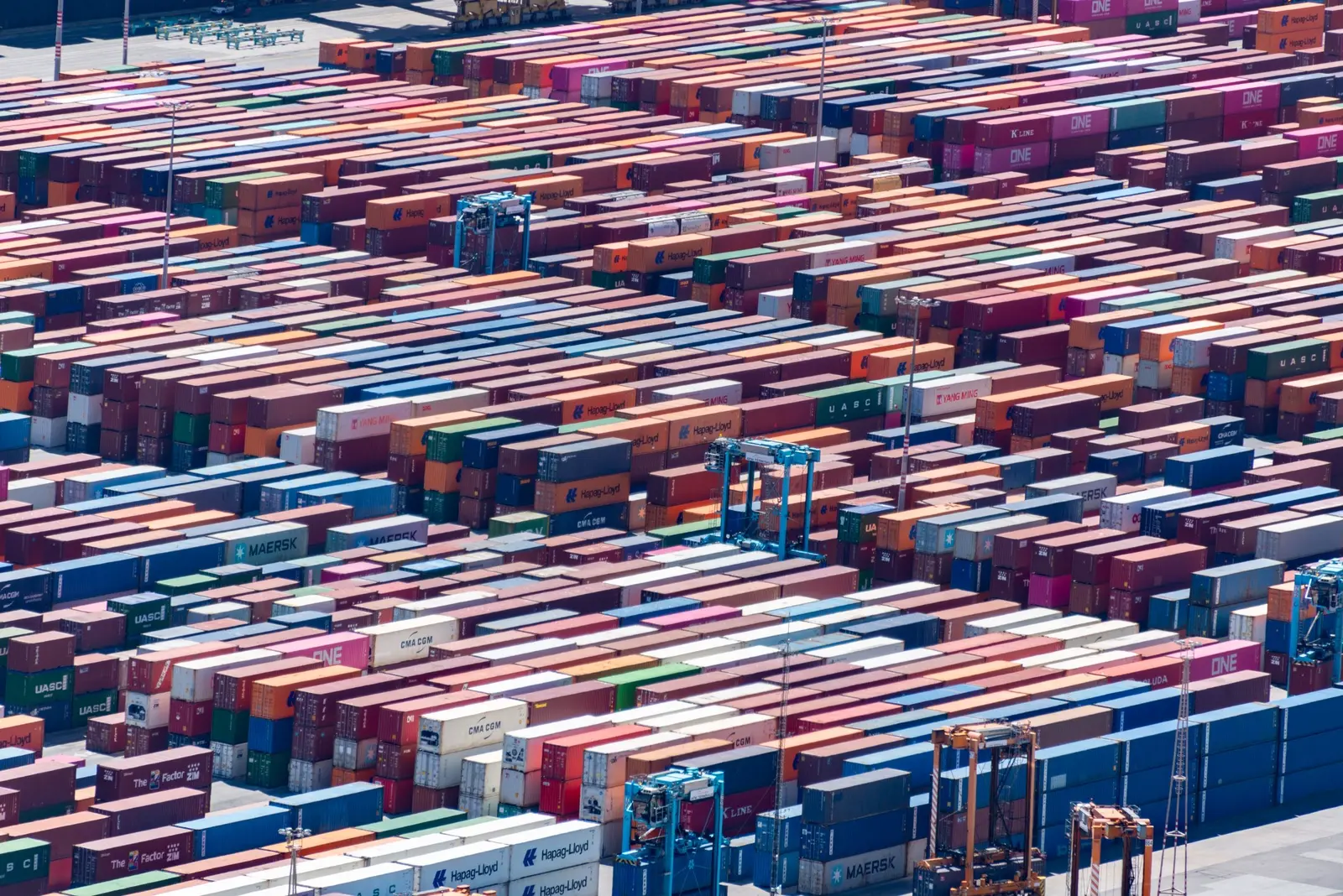 An aerial view across a container yard with handling machinery between the rows.