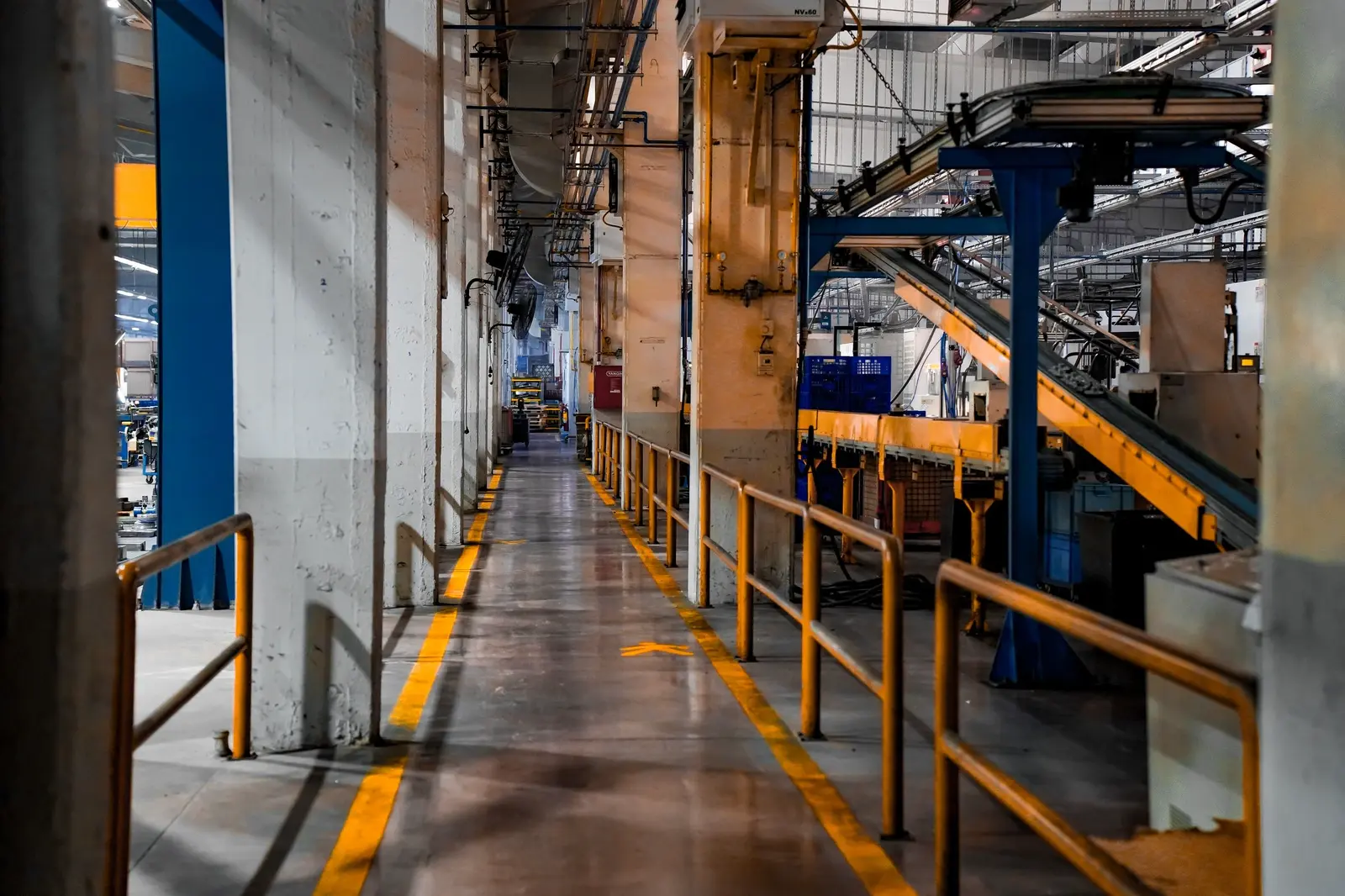 A production-plant walkway beside a conveyor line, safety rails in yellow.