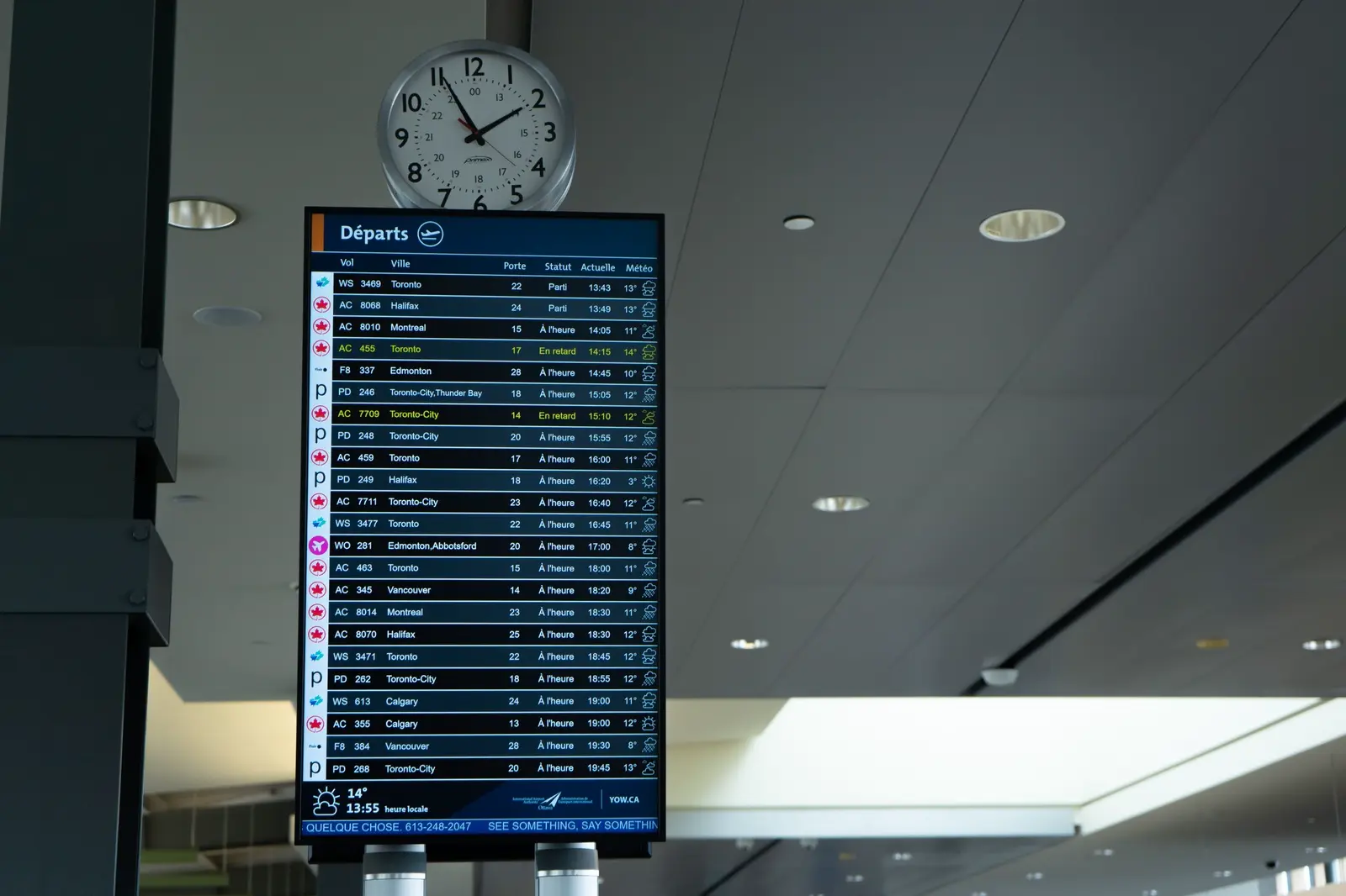 An airport departures board under a terminal clock.