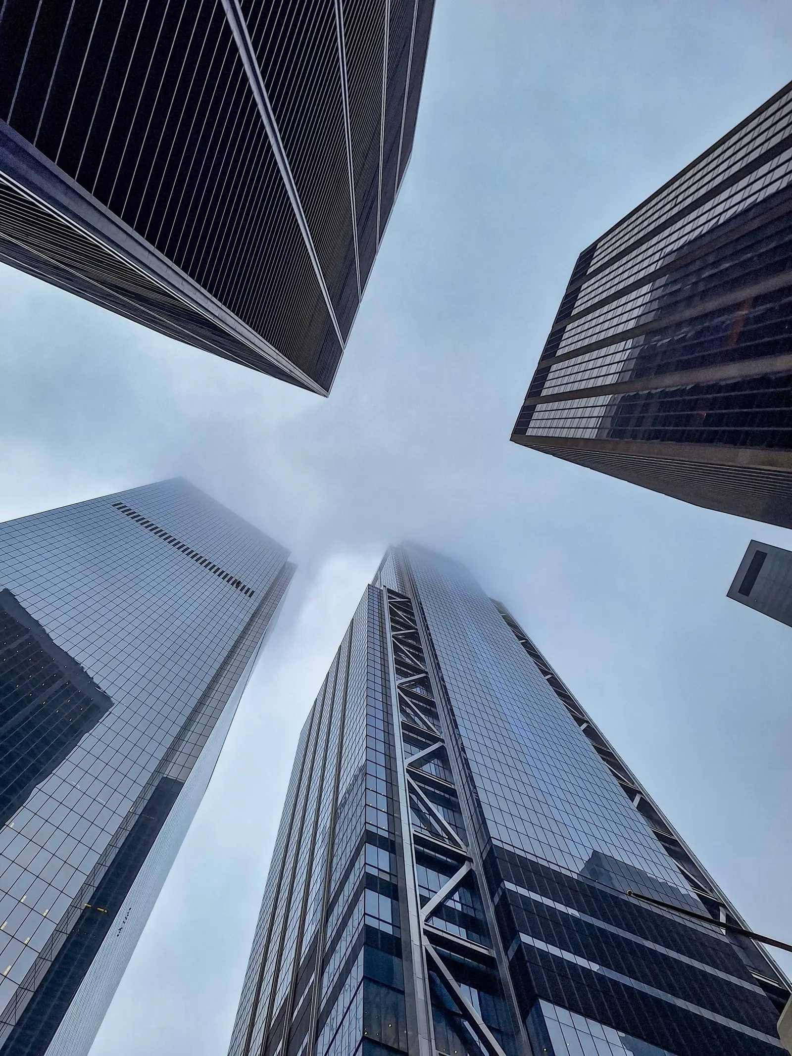 Glass towers seen from below, rising into low cloud.
