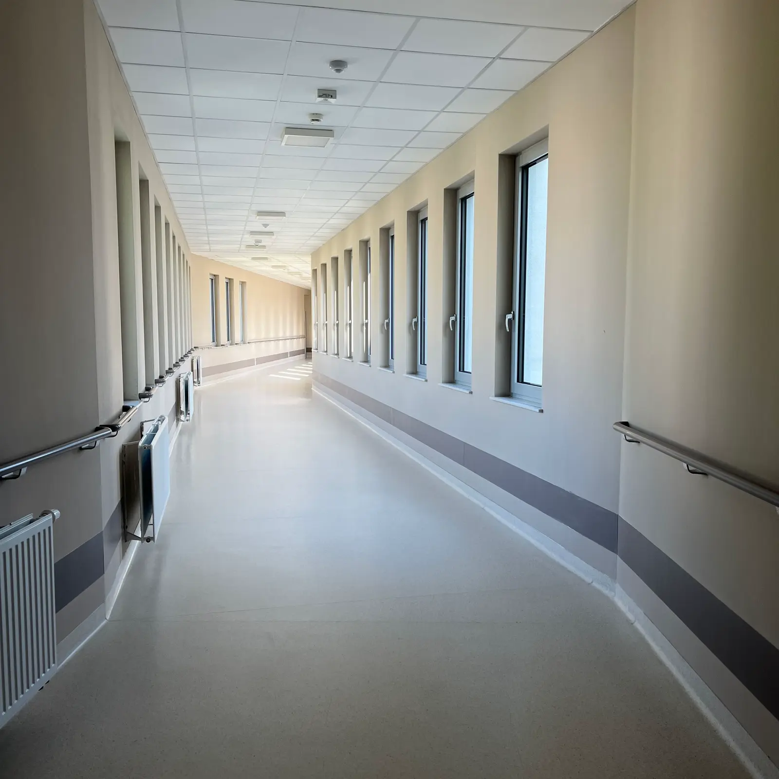 A bright, modern hospital corridor with handrails and daylight windows.