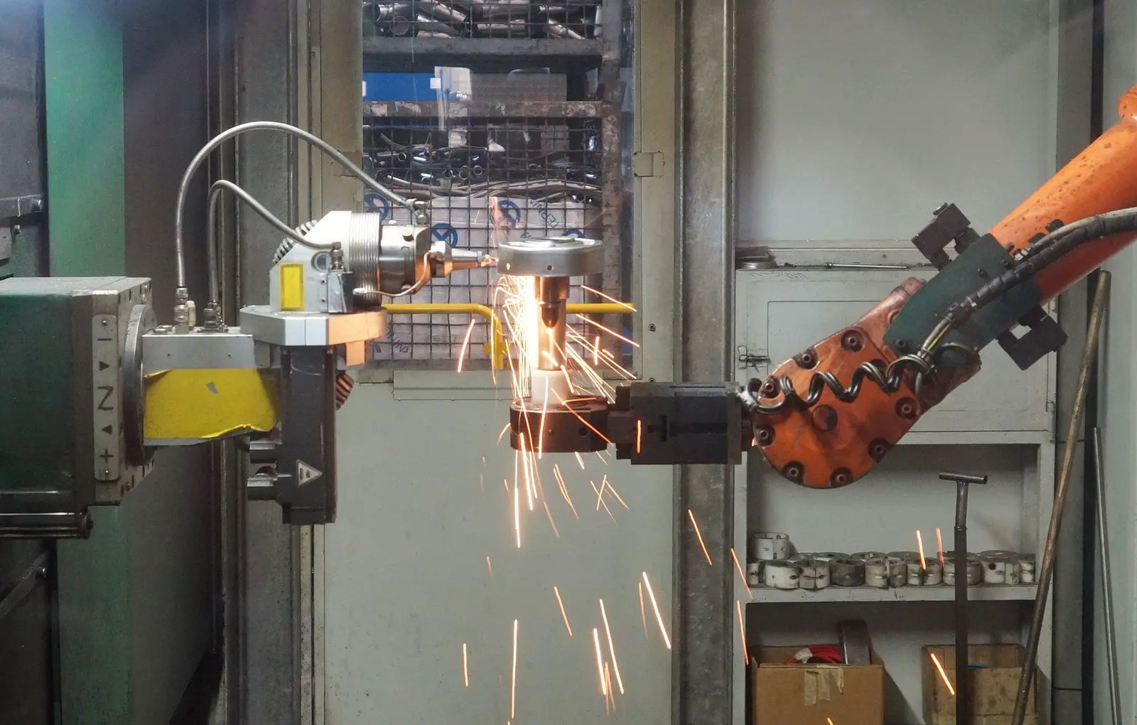An industrial robot arm grinding a steel part in a sparking work cell.