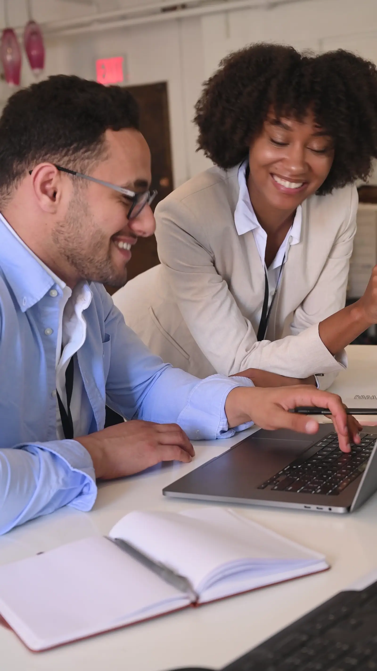 Two colleagues working through a task together at a laptop in a bright office.