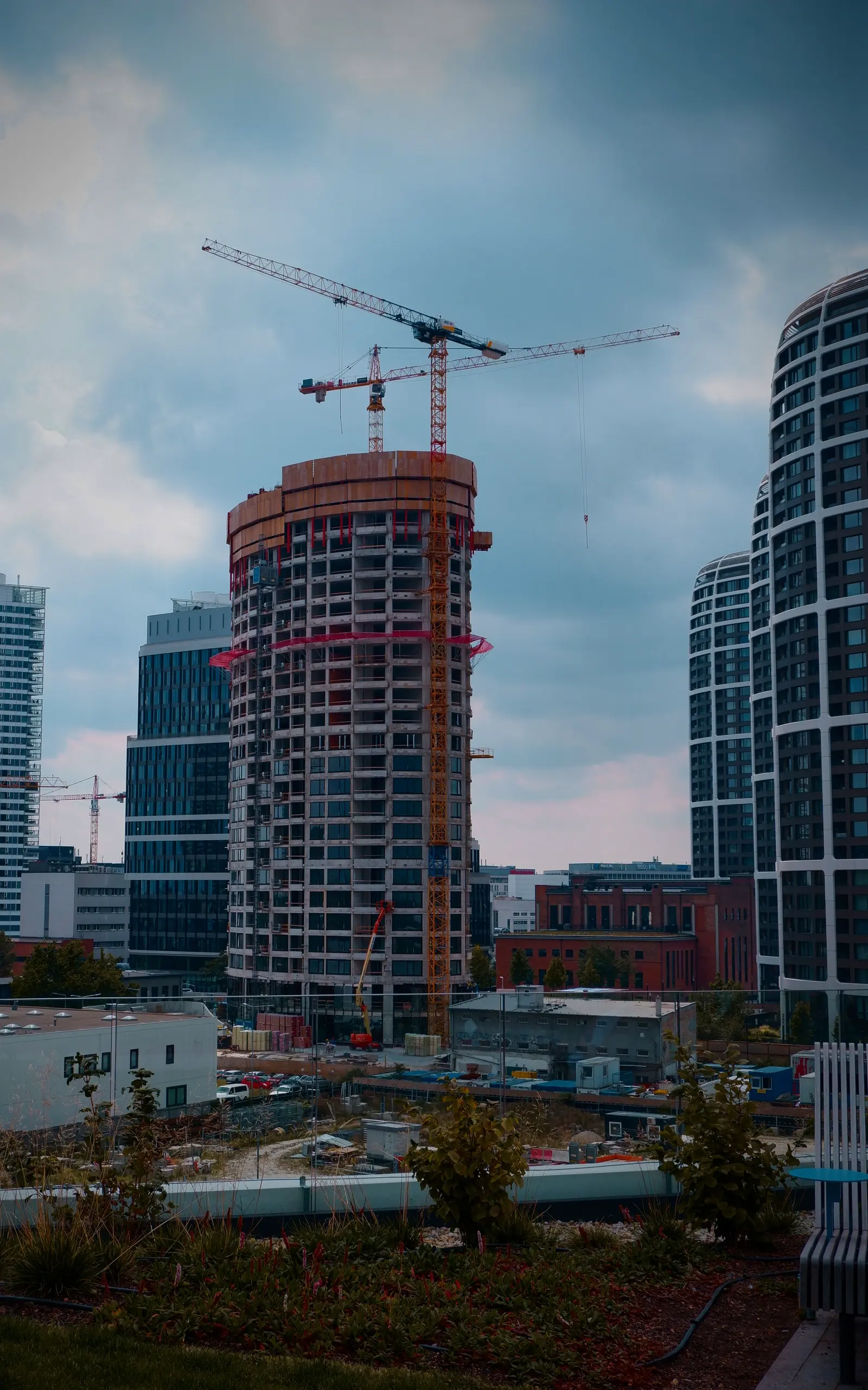 A high-rise under construction with two tower cranes above it.