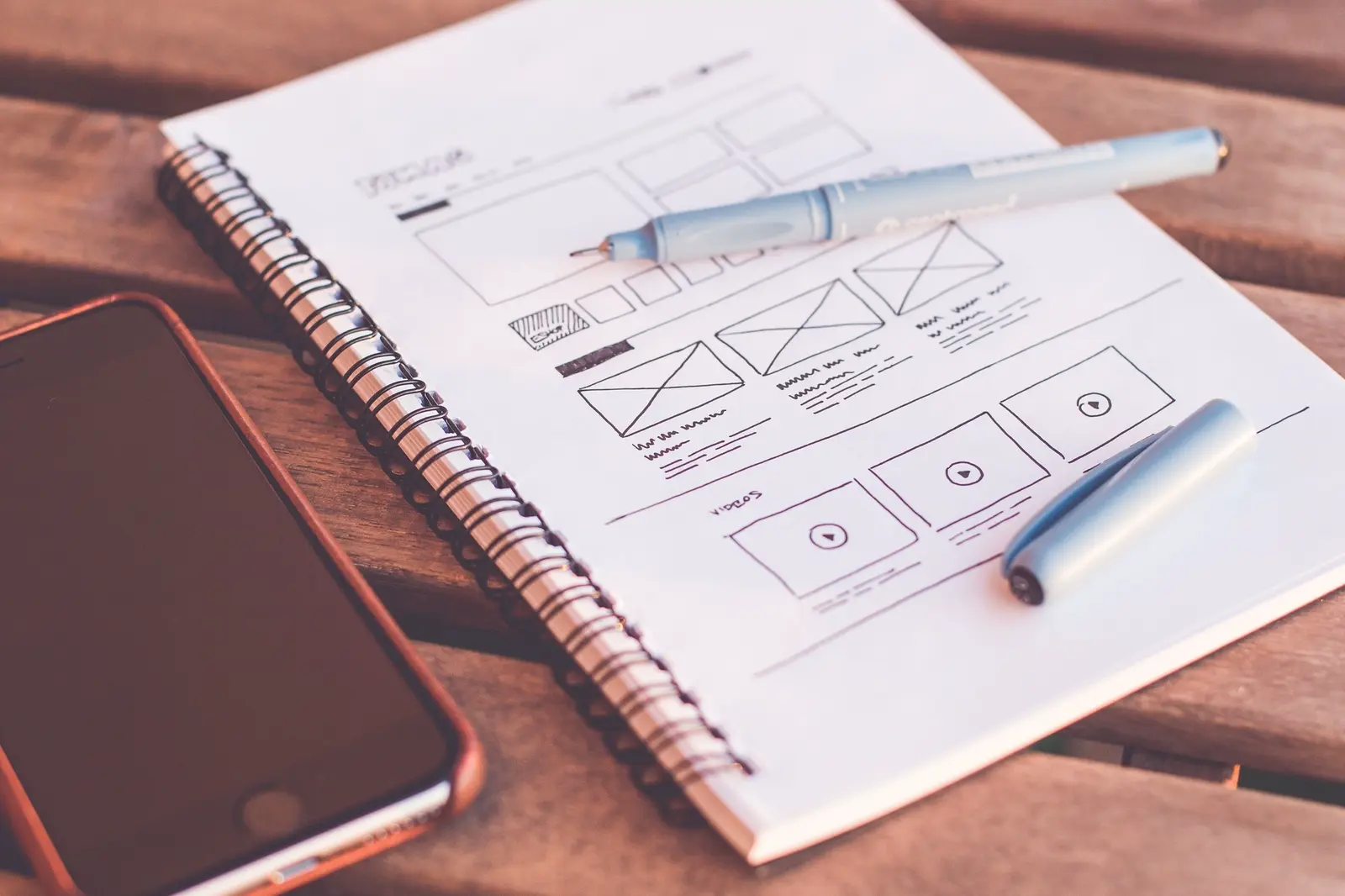 Hand-drawn application wireframes in a notebook beside a phone.